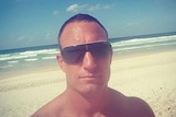 Dru Baggaley takes a selfie while wearing sunglasses on a beach.