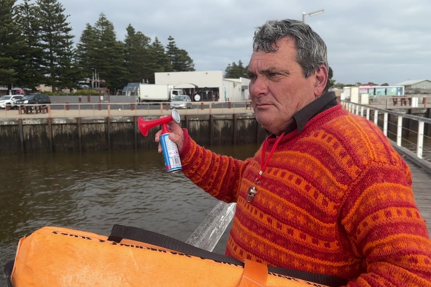 A man wearing an orange jumper and holding an airhorn and a life buoy