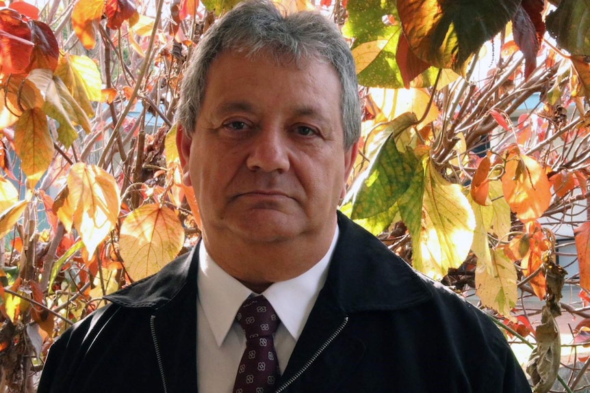 Armando Giglia standing in front of a small tree with autumn-coloured leaves.
