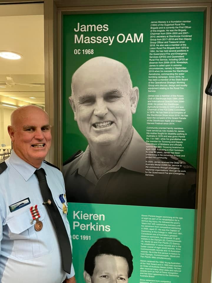 A man in official firefighter's uniform stands beside his blurb for receiving an OAM.