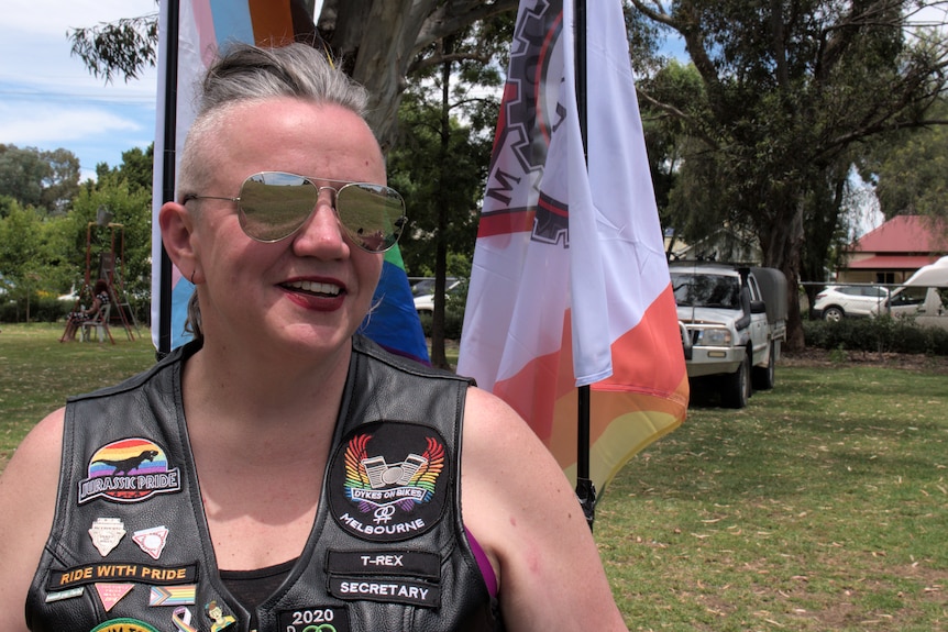 A woman wearing sunglasses smiles with flags behind her.