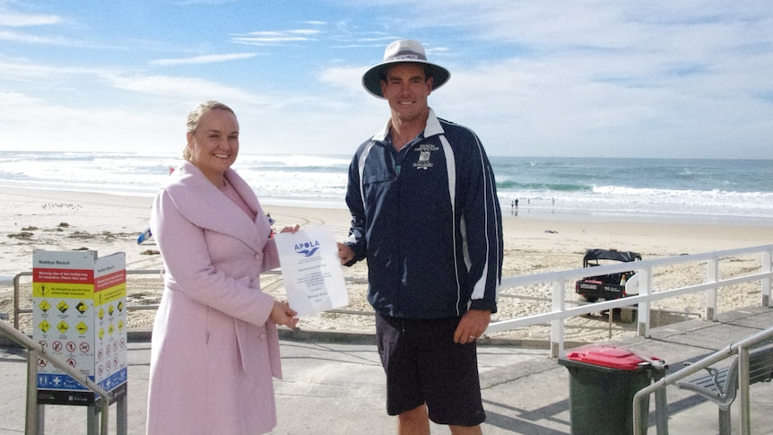 A woman hands a certificate to a lifeguard on a beach.
