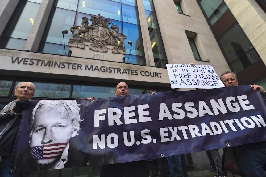 Three demonstrators hold up a banner that says "Free Assange. No U.S. extradition" outside Westminster Magistrates Court.