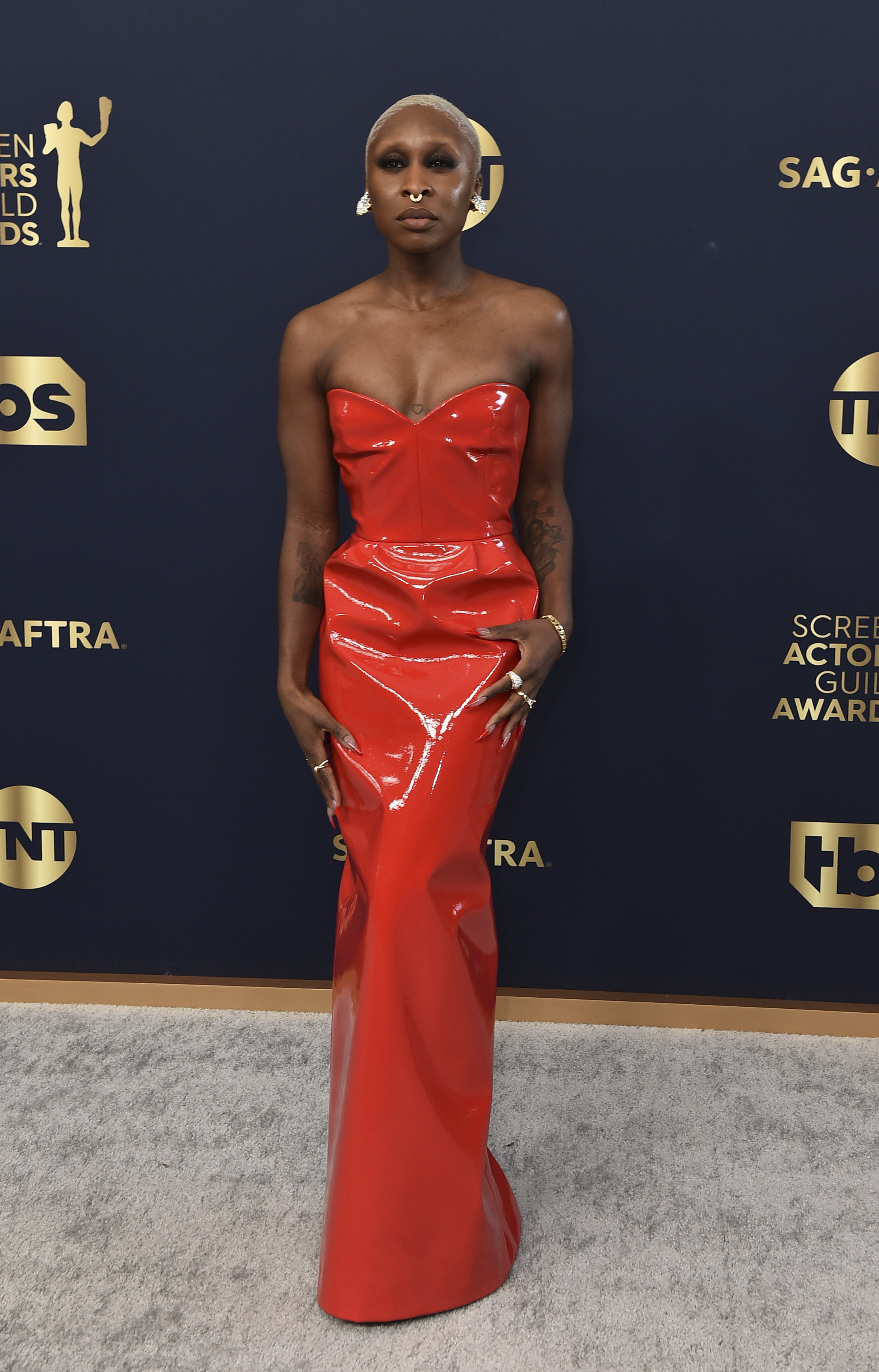 Cynthia Erivo wears a strapless floor length red gown, which looks to be made out of a plastic-based fabric. 