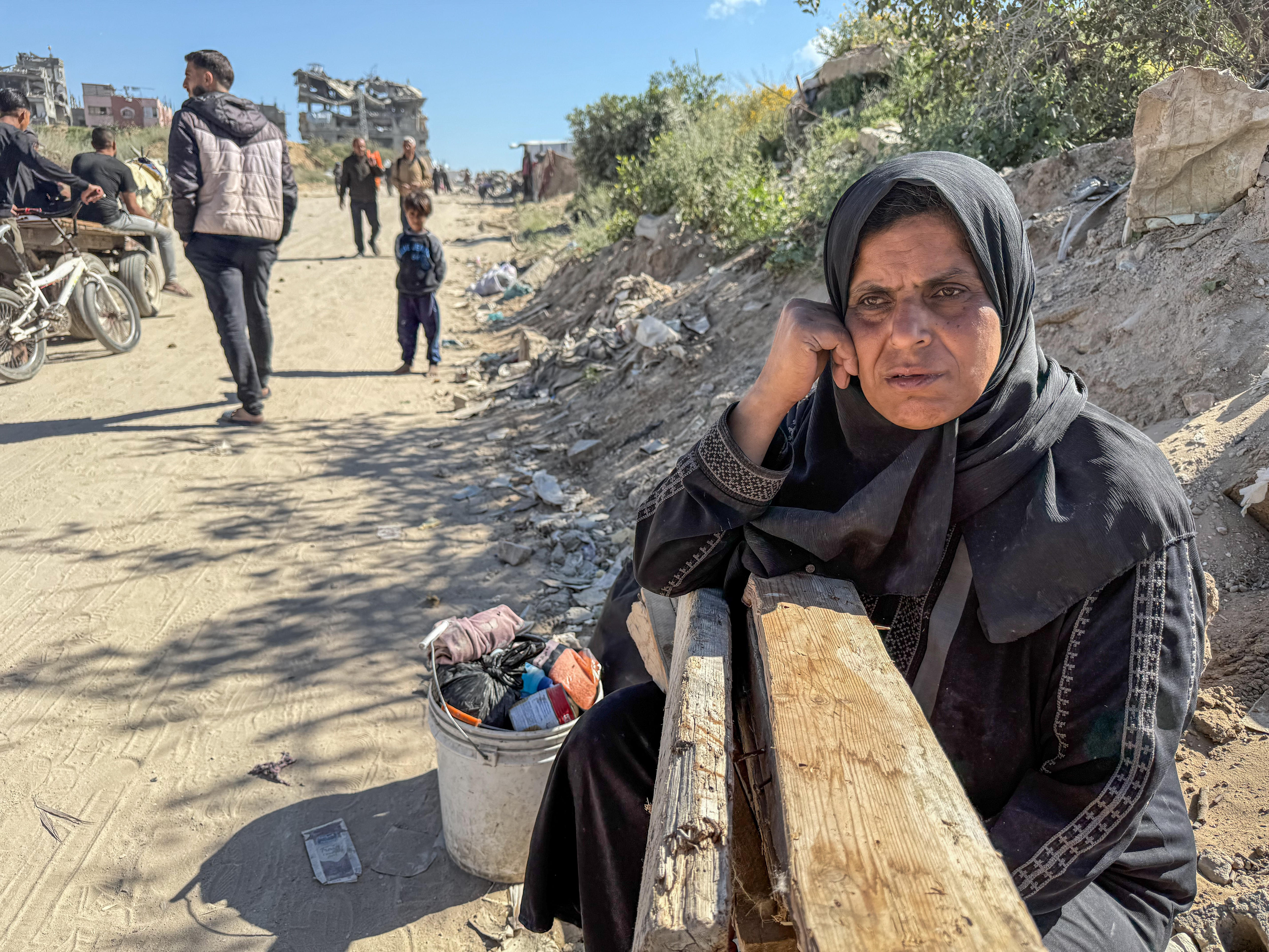 An older woman wearing a hijab on the side of a dirt path on a hill. 
