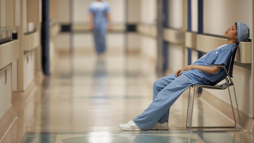 Tired doctors slumps on chair in hospital corridor.