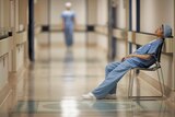 Tired doctors slumps on chair in hospital corridor.