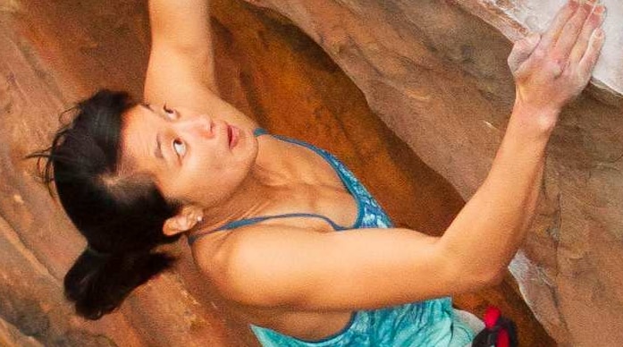 A woman in rock climbing gear climbing a ochre wall.