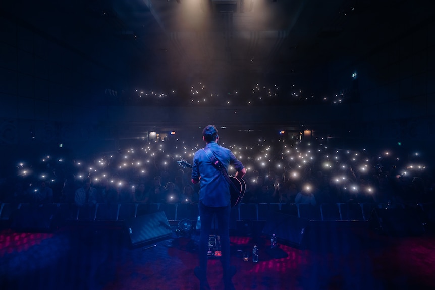 shot of the back of performer on stage at night time looking out at audience with torches