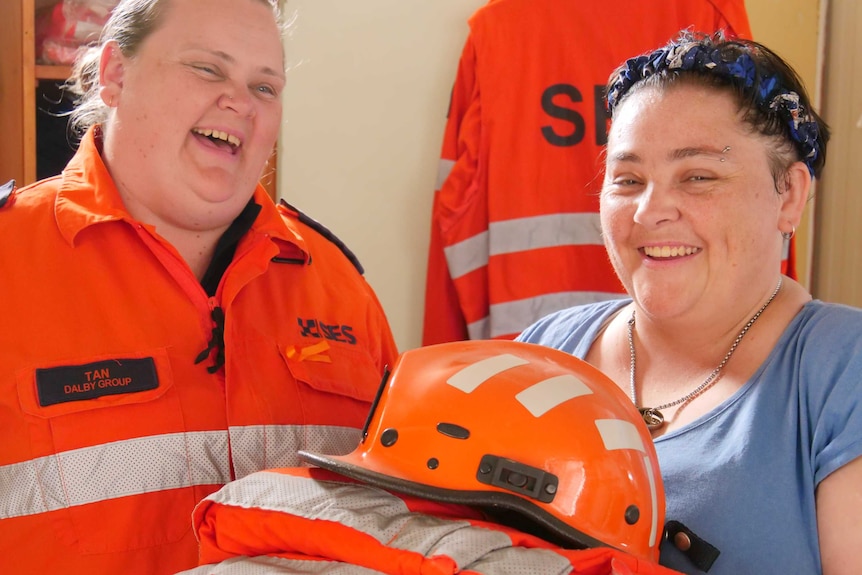 Two women laugh as they hold a stack of State Emergency Service uniforms