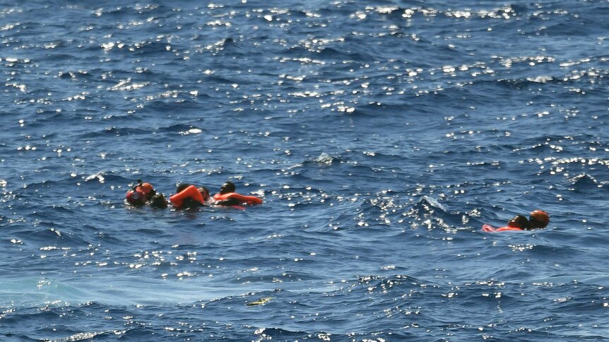 Migrants float in the water wearing life jackets after jumping off the Spanish humanitarian rescue ship Open Arms.