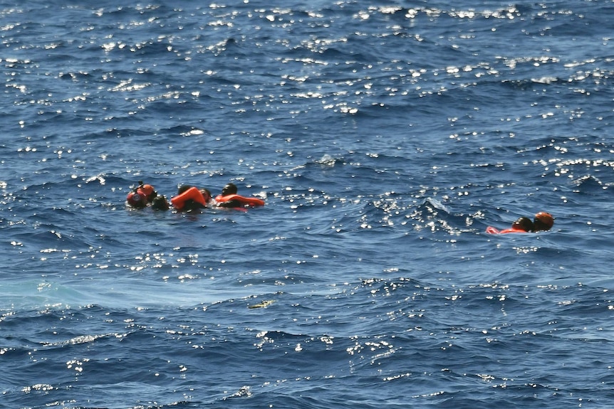 Migrants float in the water wearing life jackets after jumping off the Spanish humanitarian rescue ship Open Arms.