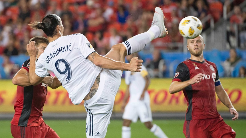 A football player with his back to the camera raises his foot at the ball with one leg still on the ground.