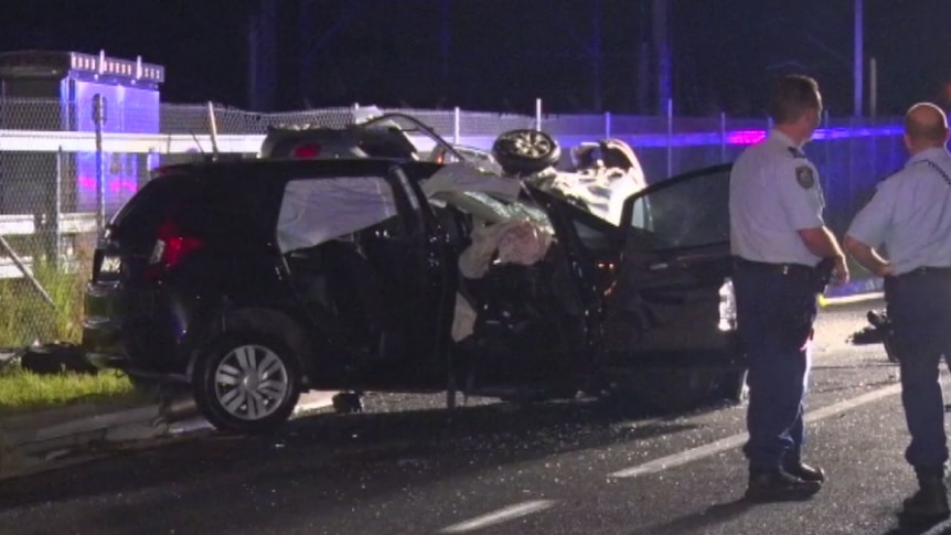 Police stand around a crashed black hatchback.