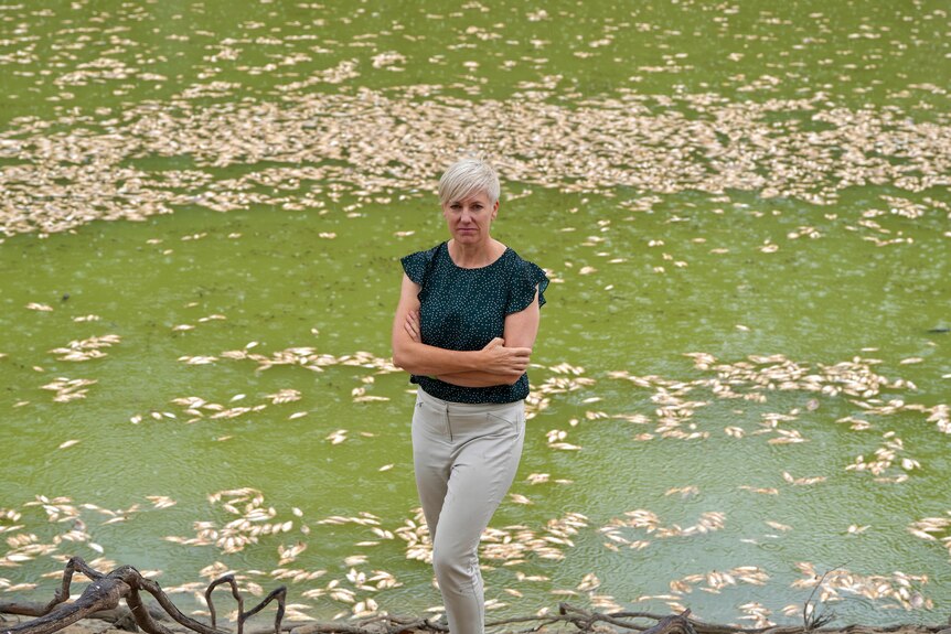 Silver-haired Greens MP Cate Faehrmann stands in front of the dead fish with her arms crossed.