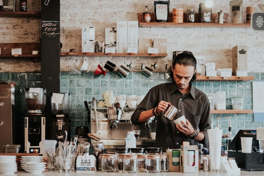 A barista pours a coffee in a rustic cafe.
