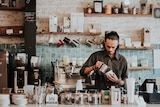 A barista pours a coffee in a rustic cafe.