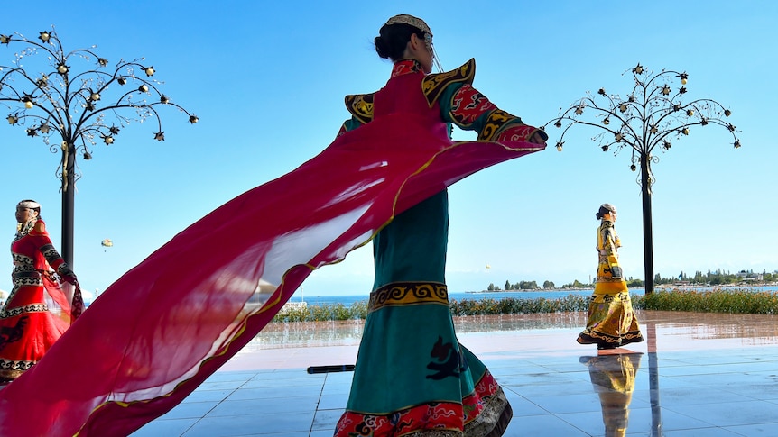 A model dressed in a designer outfit walks across blue tiles. 