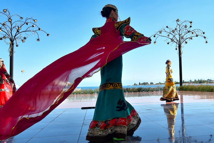 A model dressed in a designer outfit walks across blue tiles. 