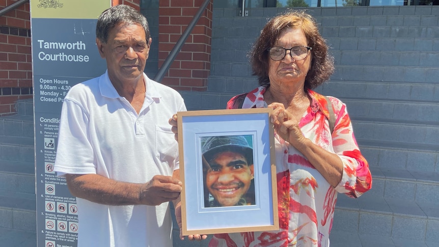 A man and woman hold up a framed photograph.