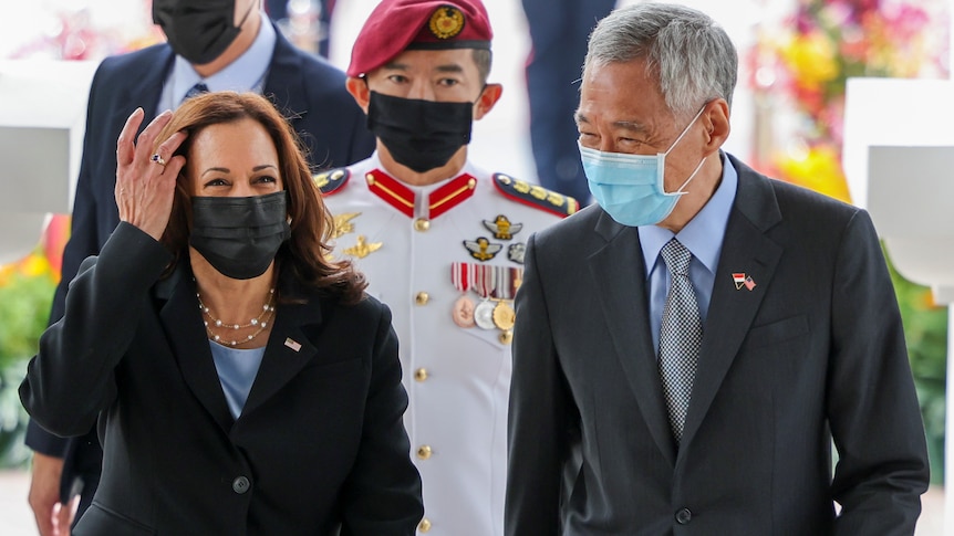 Kamala Harris walks alongside Singapore's Prime Minister Lee Hsien Loong with a uniformed local officer behind. 