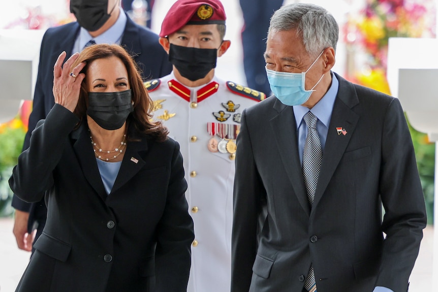 Kamala Harris walks alongside Singapore's Prime Minister Lee Hsien Loong with a uniformed local officer behind. 