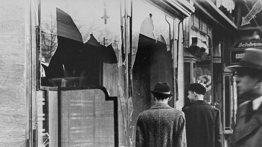 Germans walk by a Jewish business destroyed on Kristallnacht.