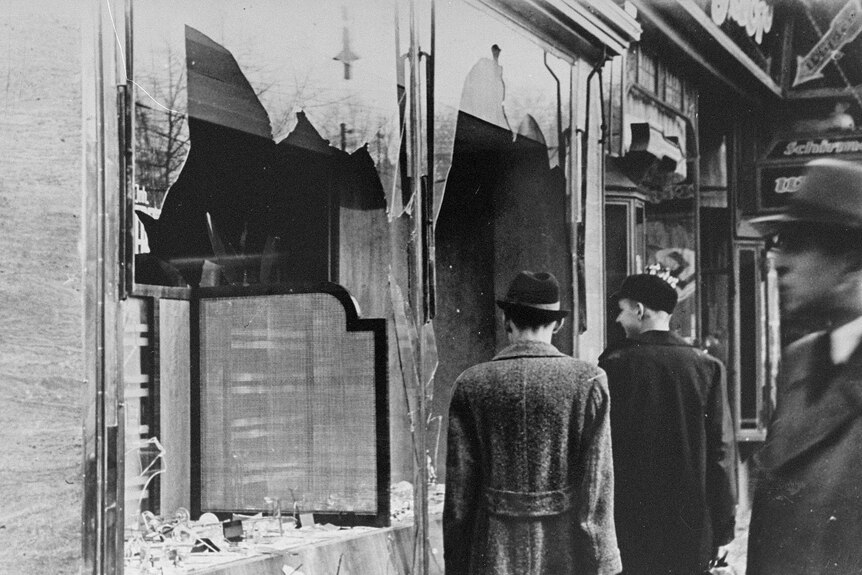 Germans walk by a Jewish business destroyed on Kristallnacht.