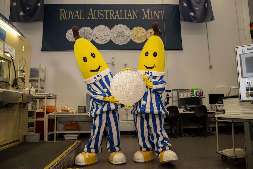 A large silver coin is held between the hands of the Bananas in Pajamas.