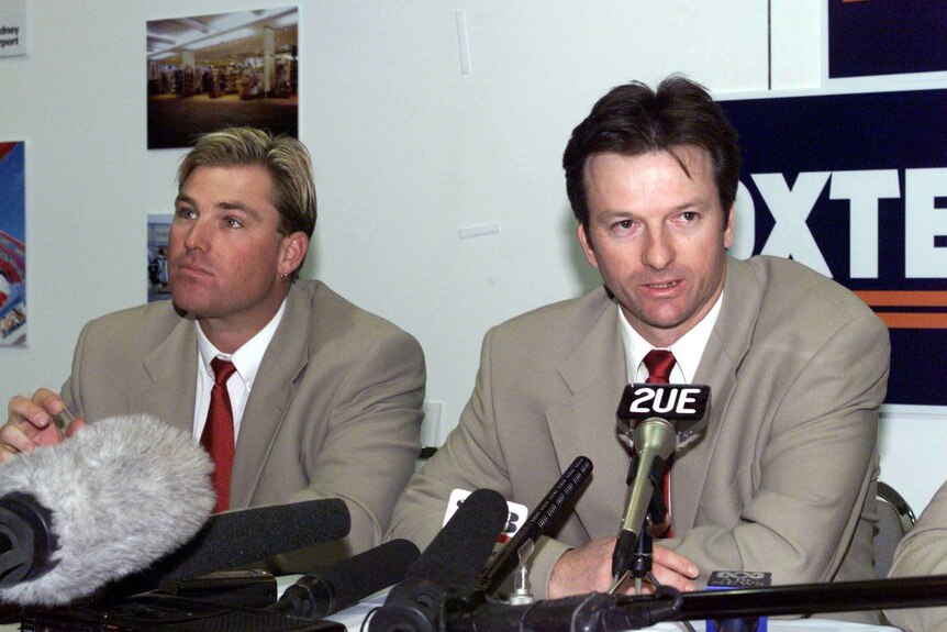 Shane Warne (left) and Steve Waugh (right) sit behind microphones at a press conference.