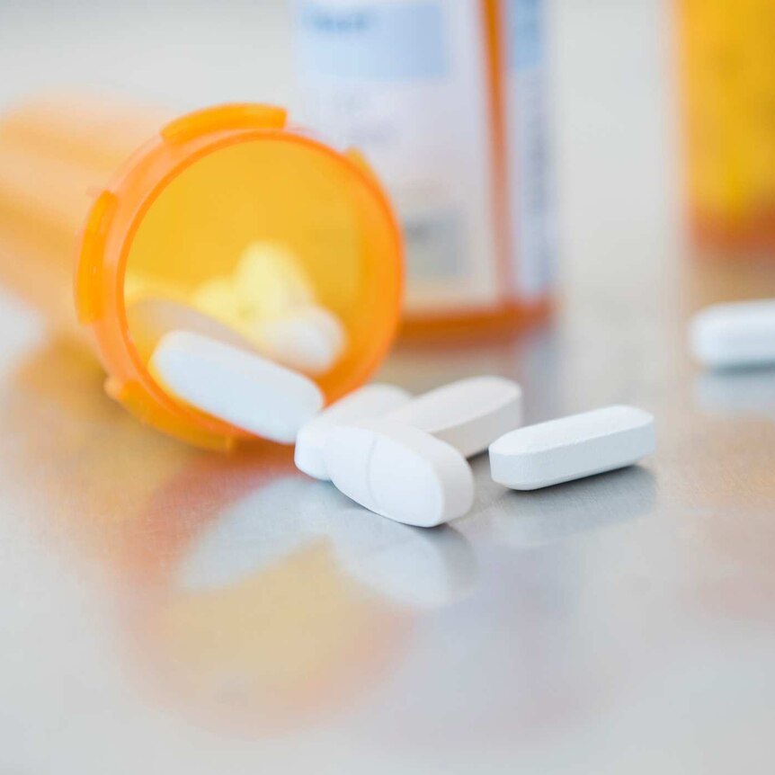 White pills in orange prescription bottle on counter.