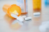 White pills in orange prescription bottle on counter.