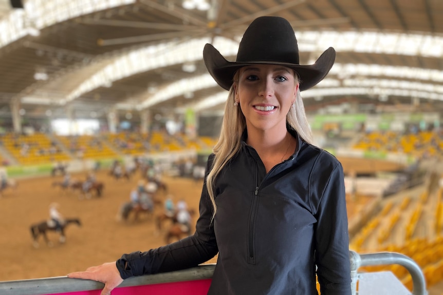 A woman stands in a black cowboy hat and black shirt.