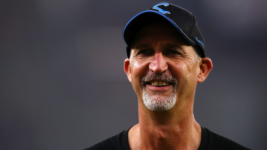 Jason Gillespie smiles while wearing a hat