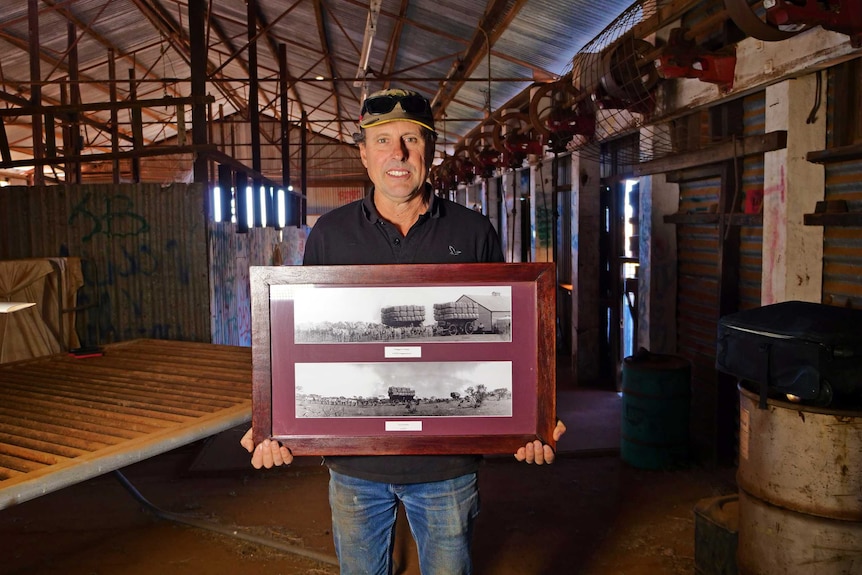 Man stands in shearing shed holding a picture in a frame