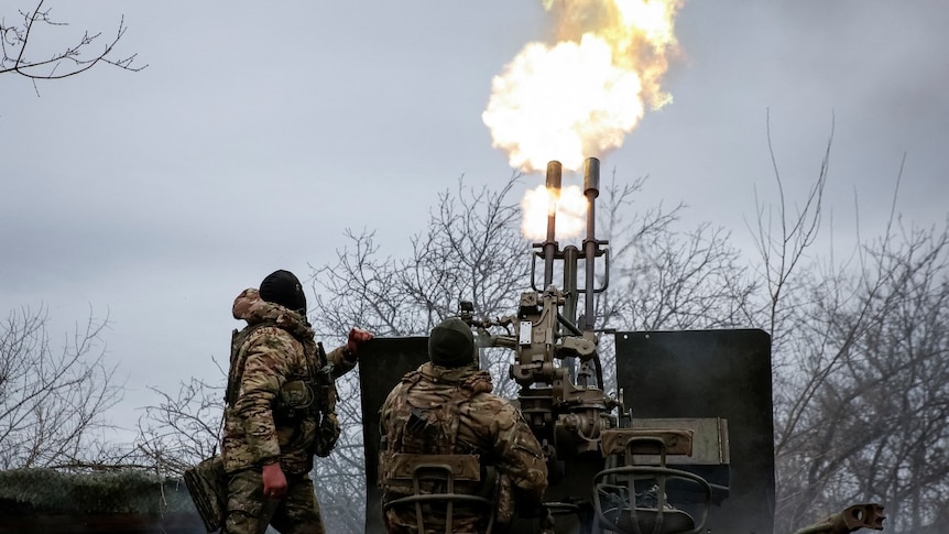 Two soldiers, with their backs to a camera, operating a large machine outdoors with flames coming out of it
