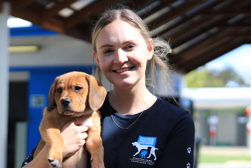 A young blonde woman holds a puppy