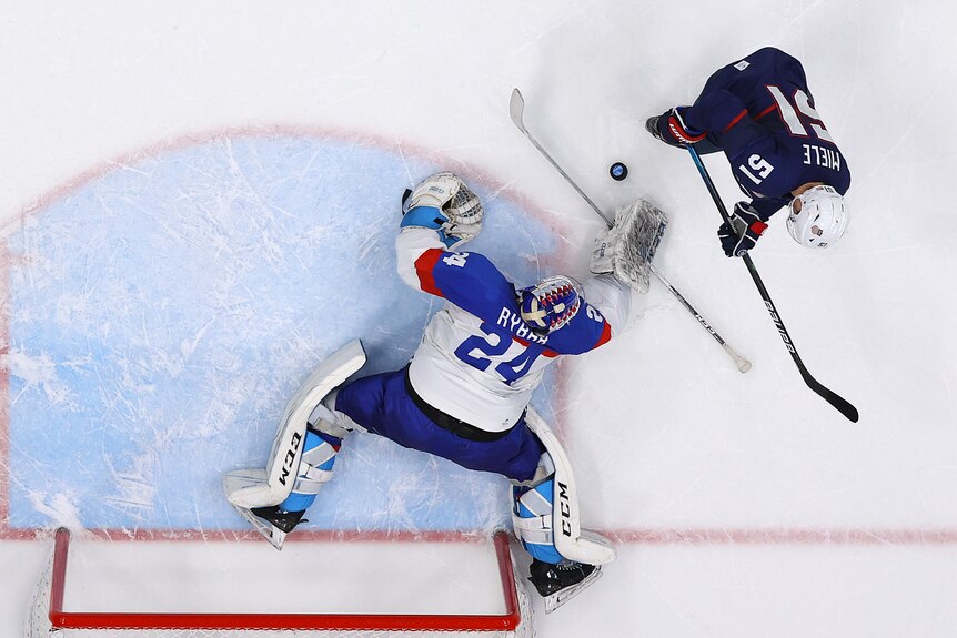 Hokejový brankár roztiahne telo, aby odrazil strelu útočníka pri krížnej streľbe na zimných olympijských hrách.