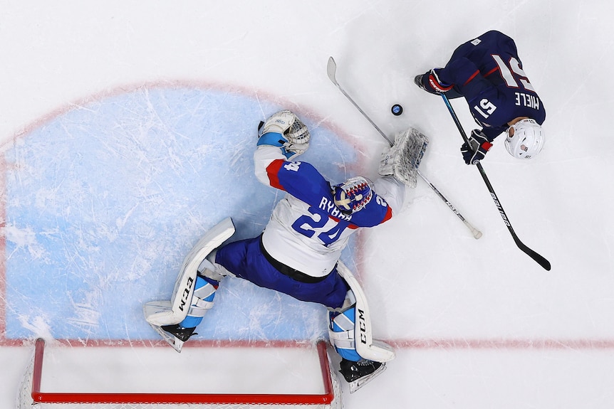 An ice hockey goaltender spreads his body to block the puck on a shot from an attacker in a shootout at the Winter Olympics.