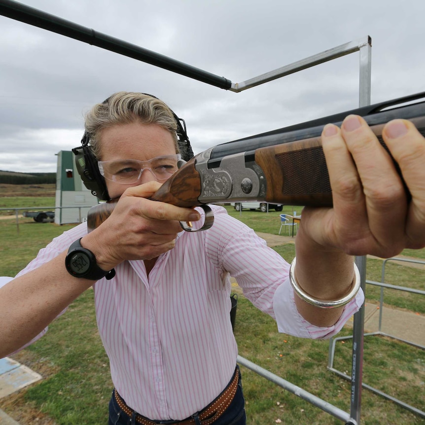 Bridget McKenzie gets ready to shoot a shotgun, looking into the sight and taking aim.