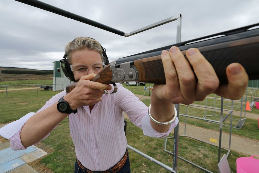 Bridget McKenzie gets ready to shoot a shotgun, looking into the sight and taking aim.