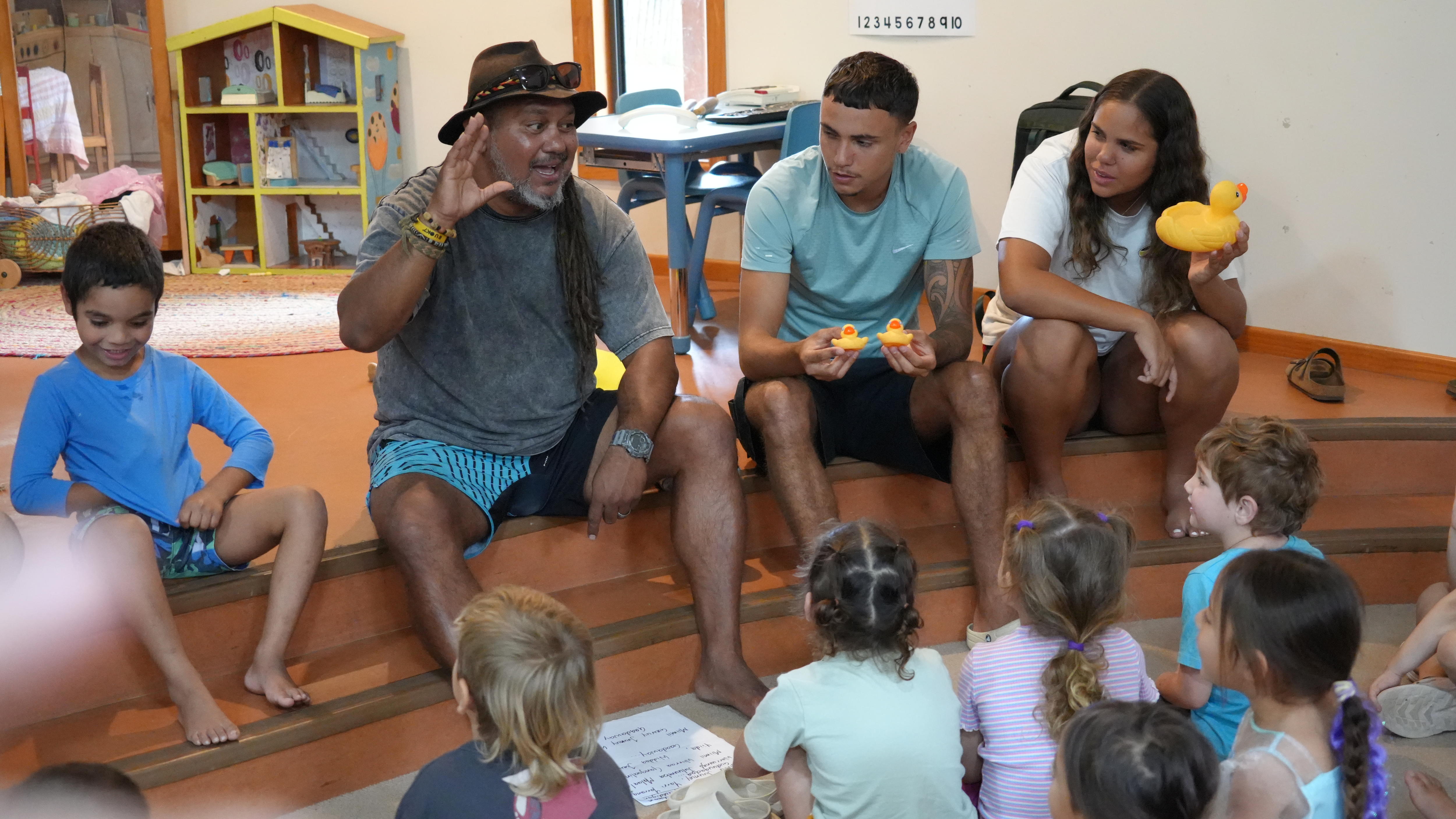 Aboriginal teachers holding rubber ducks sitting on a step with a group of kids on the floor in a preschool