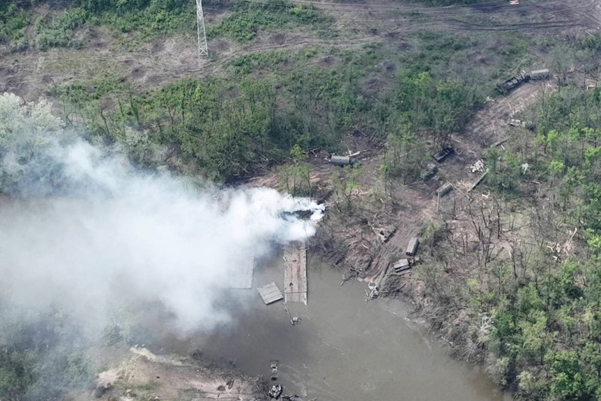 A satellite image of smoke billowing from a destroyed bridge 