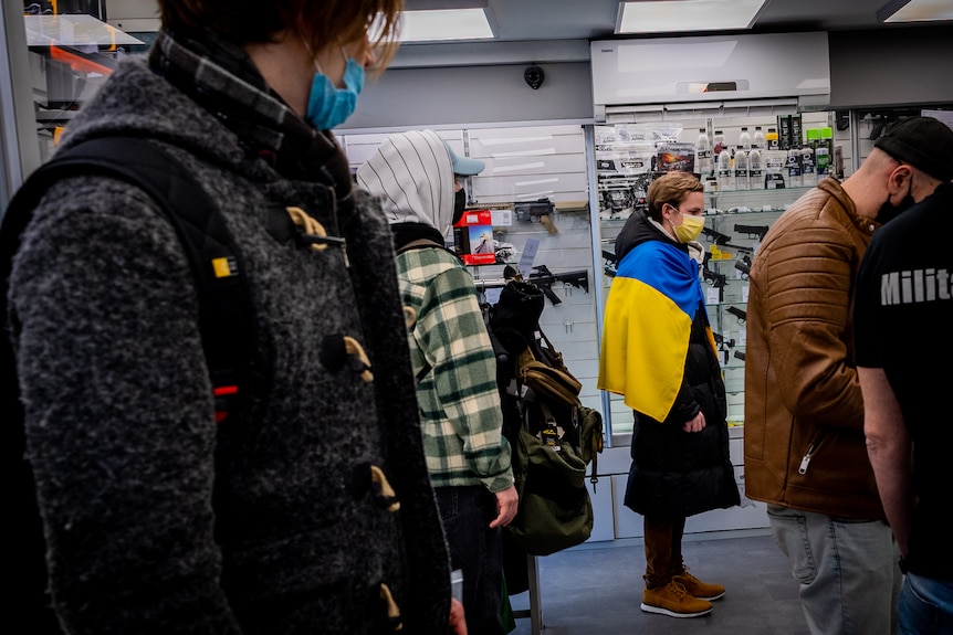 A man dressed in a Ukraninan flag stands in line for supplies.