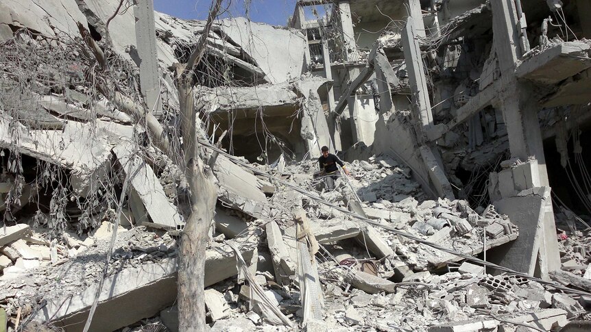A Syrian man walking on the rubble of a destroyed building