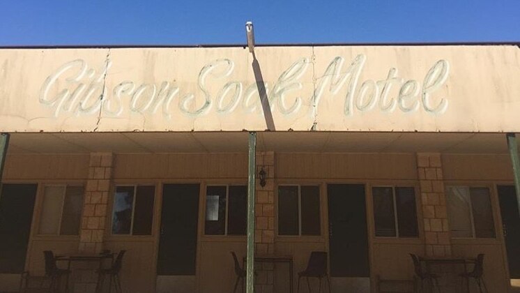 A one-storey brick motel with plastic chairs and tables out the front of each room with the sign "Gibson Soak Motel".