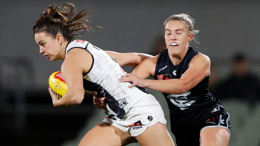 A Collingwood AFLW player holds the ball as she attempt to palm off a Carlton opponent.