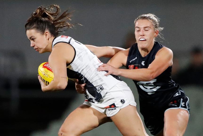 A Collingwood AFLW player holds the ball as she attempt to palm off a Carlton opponent.
