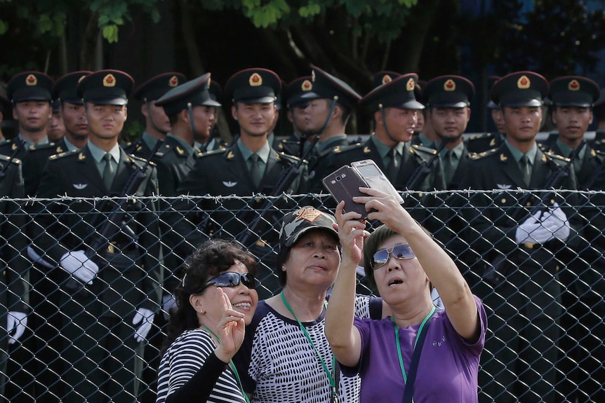 A group of three women, who are visitors, take a selfie in front of Chinese soldiers in Hong Kong