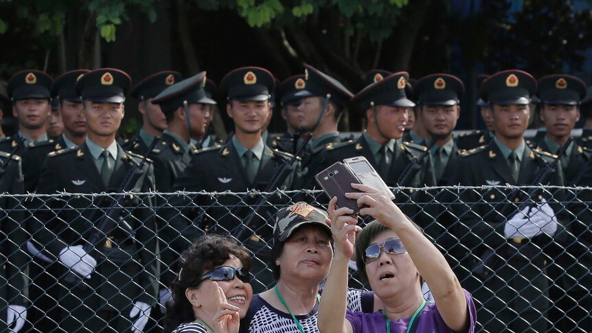 A group of three women, who are visitors, take a selfie in front of Chinese soldiers in Hong Kong